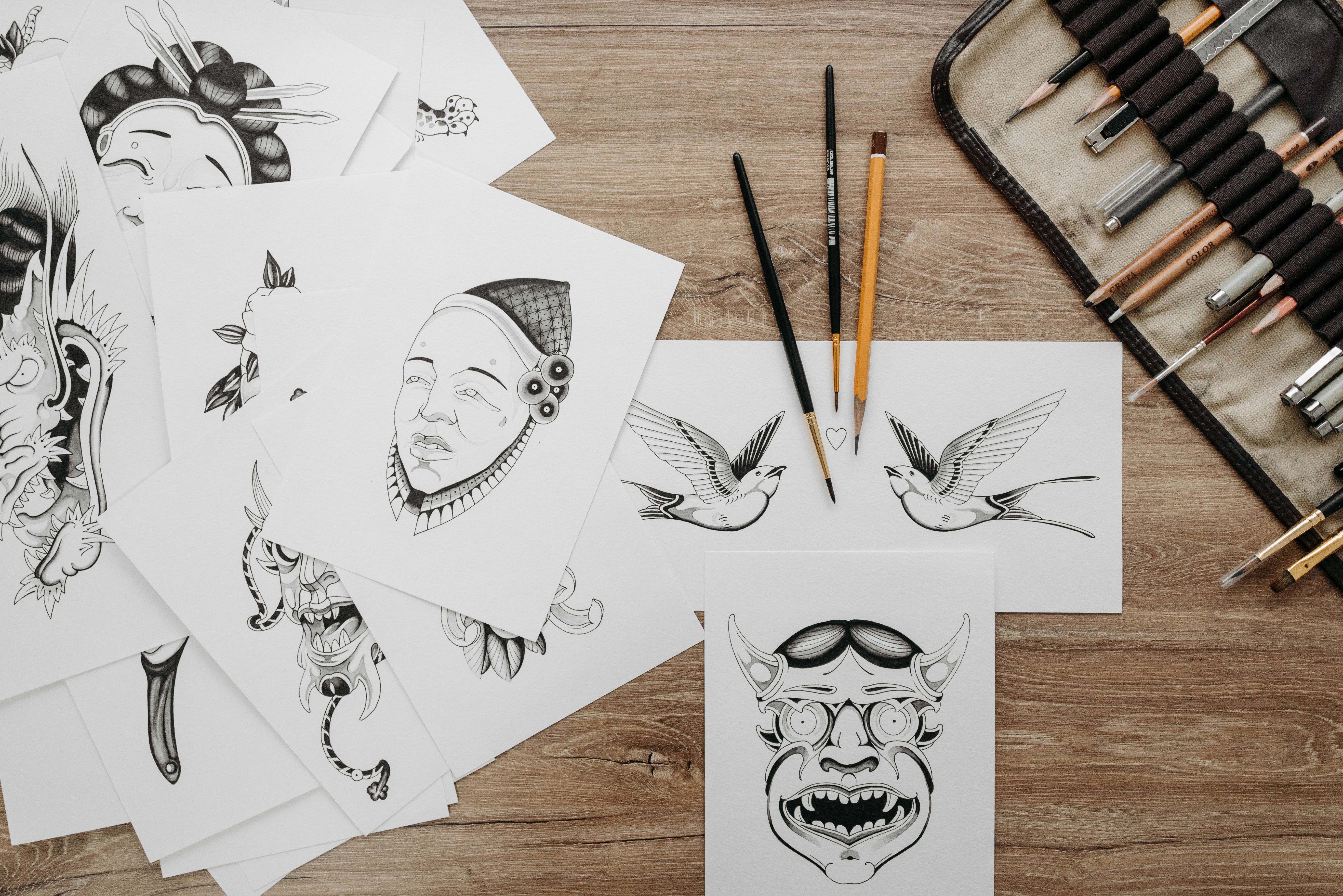 Flash sheets japoneses com geisha e máscara oni sobre mesa com pincéis de tatuador